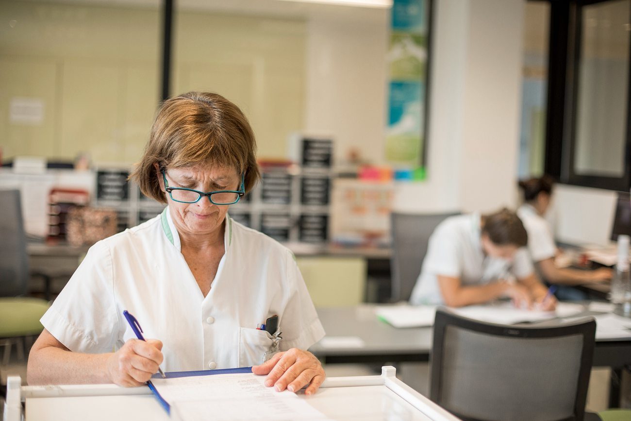 Zorgverlener die aan een bureau schrijft, met collega's aan het werk op de achtergrond
